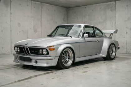 BMW 3.0 CSL coupé argenté polaris dans un garage minimaliste en béton, vue 3/4 avant avec spoilers aérodynamiques et jantes BBS d'époque