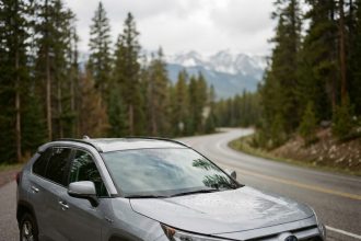SUV hybride argent garé sur une route de montagne entourée de sapins, vue trois-quarts avant
